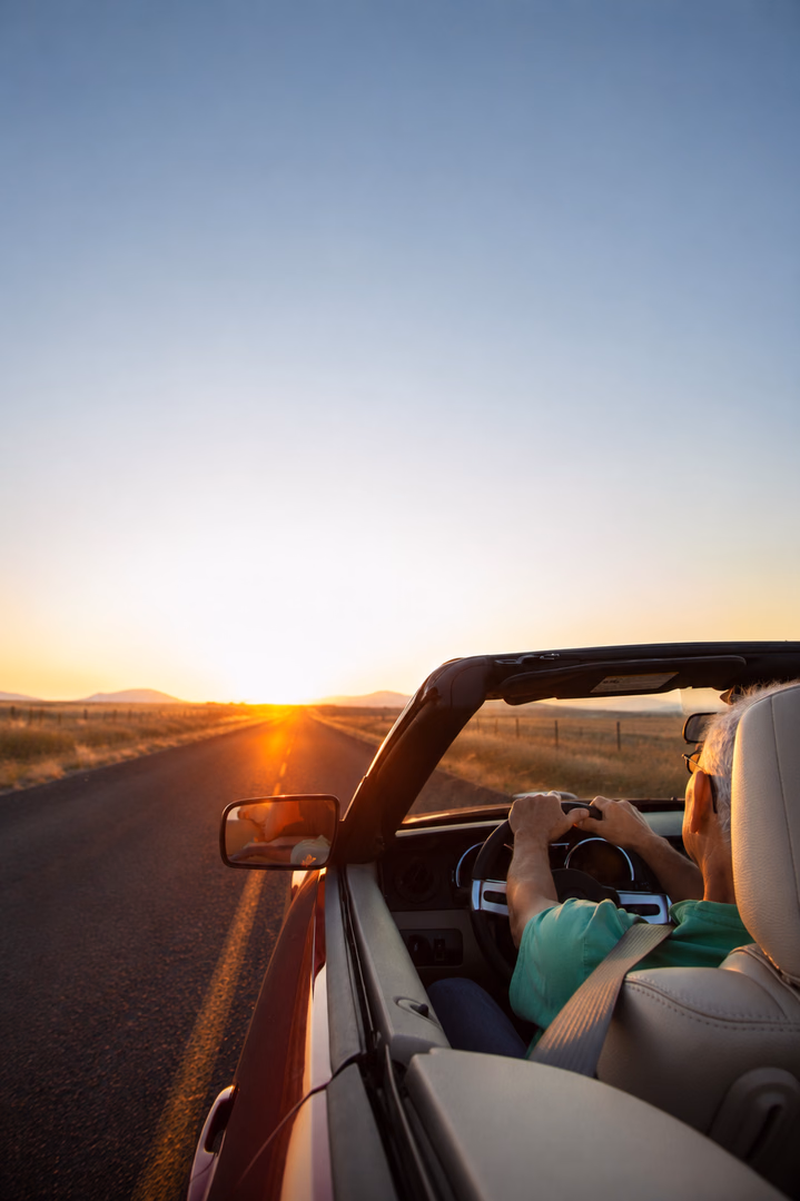 Mann fährt bei Sonnenuntergang in einem Cabriolet über eine Landstraße
